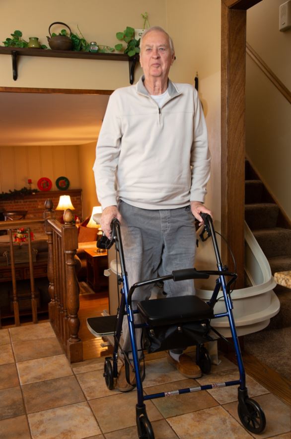 man holding onto walker for support as he gets out of stair lift chair